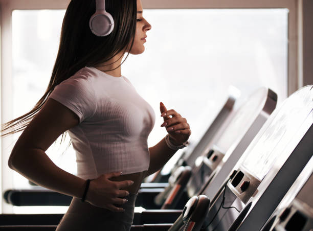 Beautiful young woman doing workout in gym. Pretty young woman working out. In leggins and sport outfit. Listening music on wireless headphones.Doing squats and lifting weights. A person exercising on a treadmill or doing yoga. stock pictures, royalty-free photos & images