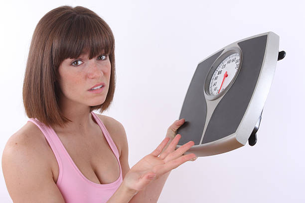 girl unhappy with her scale fit young girl holding scale not satisfied with the results  A person looking at a scale with a concerned expression on their face. stock pictures, royalty-free photos & images